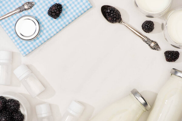 Top view of bottles and glasses of homemade yogurt, teaspoons, berries and containers with starter cultures on white 