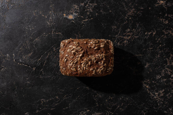 top view of fresh baked brown bread loaf with sunflower seeds on stone black surface