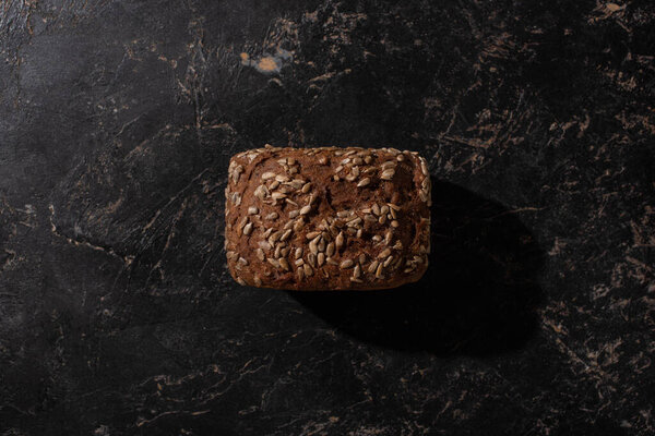верхний вид свежего бурого хлеба с семенами подсолнечника на каменной черной поверхности
