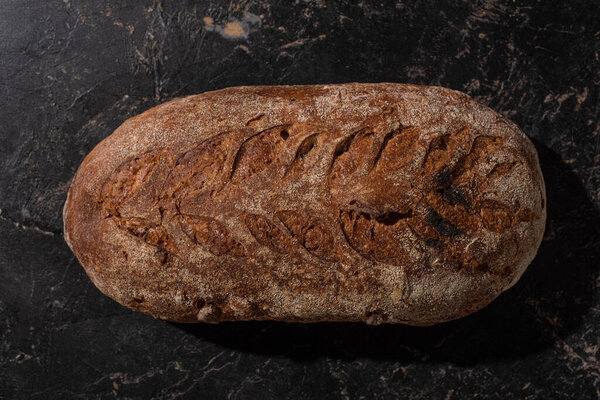 top view of fresh baked brown bread loaf on stone black surface