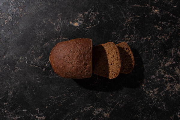 top view of fresh cut loaf of brown bread on stone black surface