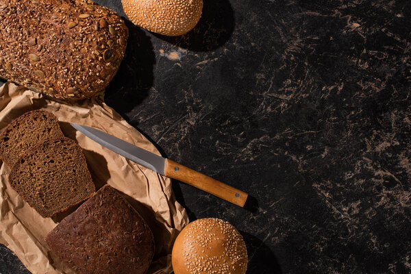 top view of fresh cut and whole bread with knife on stone black surface