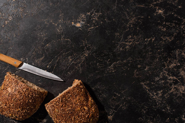 top view of cut whole grain bread with knife on stone black surface