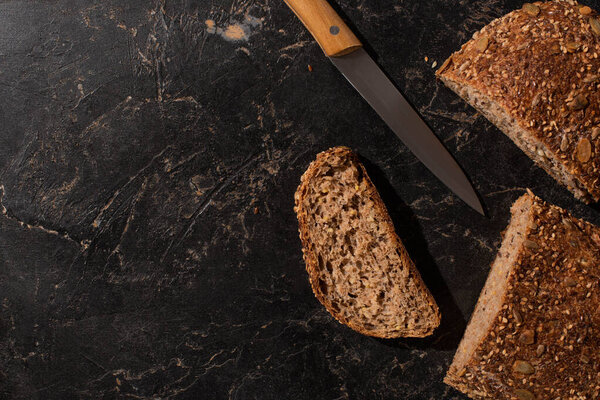 вид сверху на разрезанный хлеб из цельного зерна и нож на каменной черной поверхности

