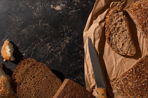 纸上切面全麦面包的头像接近石色表面的刀片 — 图库照片