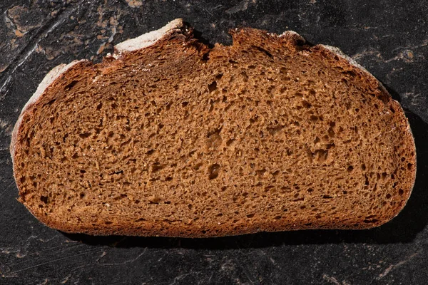 Kaya Gibi Siyah Yüzeyde Kahverengi Ekmek Diliminin Üst Görüntüsü — Stok fotoğraf