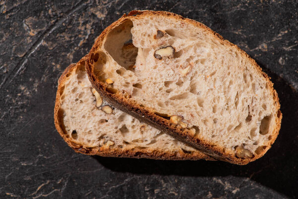 top view of fresh whole grain bread slices with nuts on stone black surface