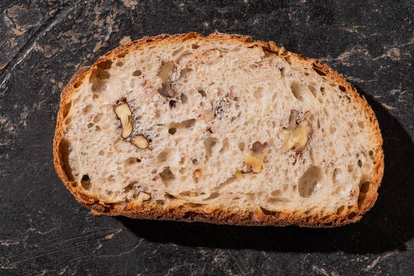 top view of fresh whole grain bread slice with nuts on stone black surface