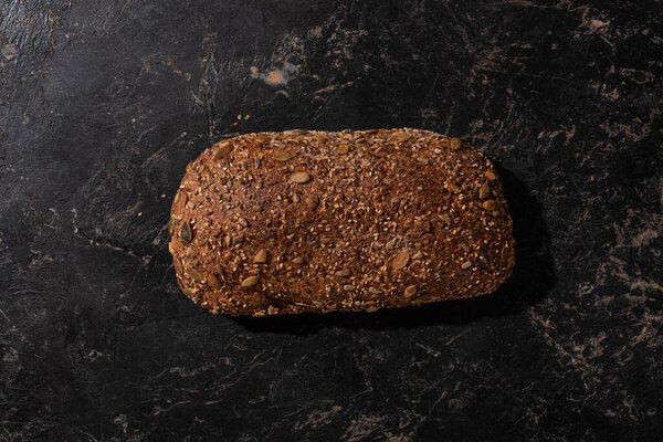 top view of fresh baked loaf of whole grain bread on stone black surface