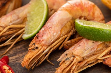 close up view of fried shrimps with chili and lime on wooden board clipart