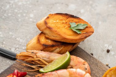 close up view of fried shrimps with grilled toasts and lime on wooden board on grey concrete background clipart