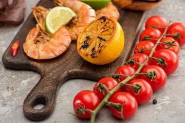 Limonlu ve limonlu kızarmış karidesleri ahşap tahtada, çimentoda, kiraz domateslerinin yanında, gri arka planda.