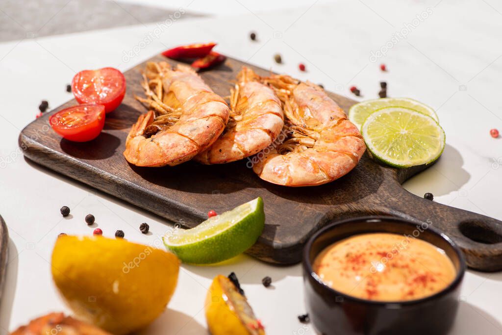 selective focus of fried shrimps on wooden board near lemon, sauce and lime on white background