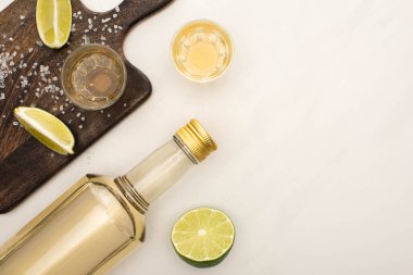 Limonlu altın tekila manzarası, beyaz mermer yüzeyde ahşap kesim tahtası.