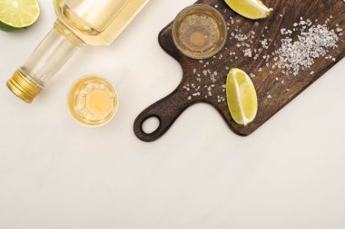 Limonlu altın tekila manzarası, beyaz mermer yüzeyde ahşap kesim tahtası.