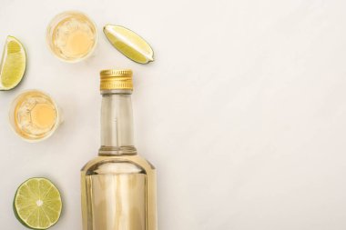 Şişede altın tekila ve beyaz mermer yüzeyde limonlu shot bardakları.