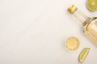 Şişede altın tekila ve beyaz mermer yüzeyde misket limonlu bardak manzarası.