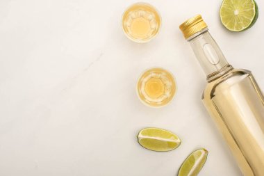 Şişede altın tekila ve beyaz mermer yüzeyde limonlu shot bardakları.
