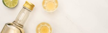 Şişede altın tekila ve beyaz mermer yüzeyde limonlu shot bardakları, panoramik çekim