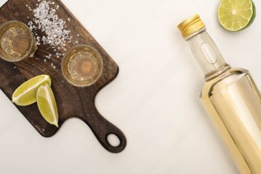 Limonlu altın tekila manzarası, beyaz mermer yüzeyde ahşap kesim tahtası.