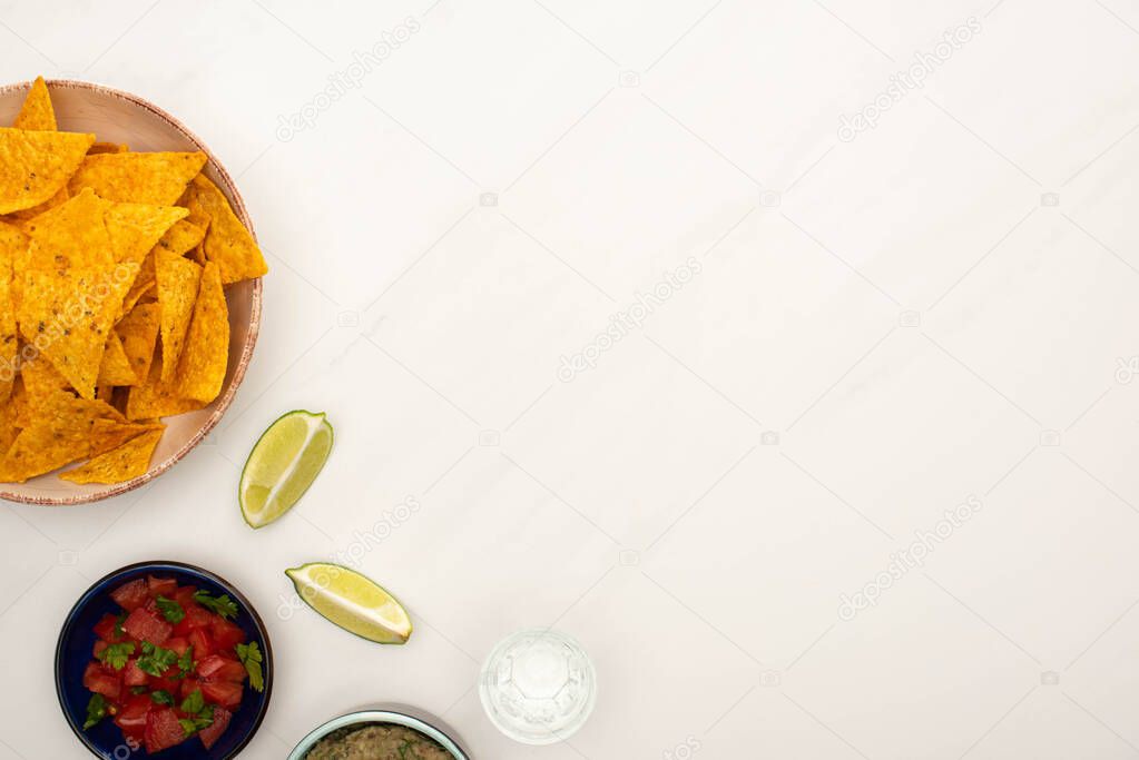 top view of tequila with lime, chili pepper and nachos in plate on white marble surface