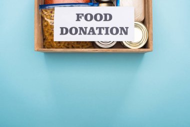 Kutuların ve inlemelerin üst görüntüsü mavi arka planda gıda bağışı yazılı kartın yanındaki tahta kutuda.