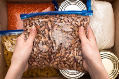 cropped view of woman holding  beans in zipper bag, food donation concept clipart