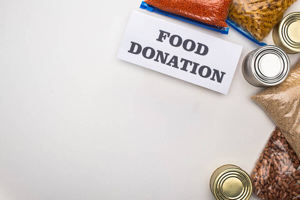 top view of cans and groats in zipper bags near card with food donation lettering on white background