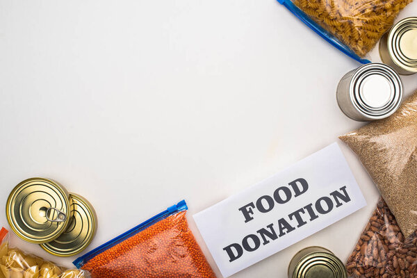 top view of cans and groats in zipper bags near card with food donation lettering on white background
