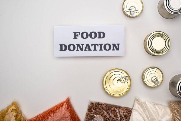 top view of cans and groats in zipper bags near card with food donation lettering on white background