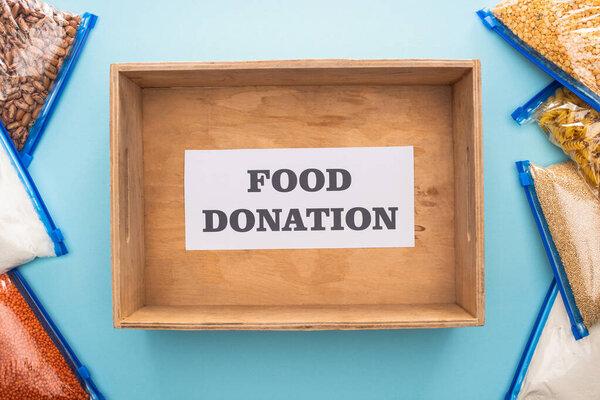 верхний вид крупы в мешках-молниях рядом с деревянной коробкой с карточкой с надписью о пожертвовании еды на синем фоне
