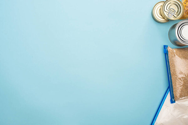 top view of cans and groats in zipper bags on blue background