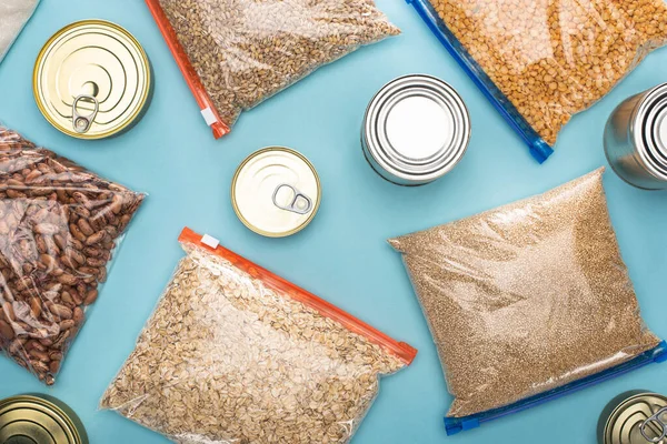top view of cans and groats in zipper bags on blue background, food donation concept