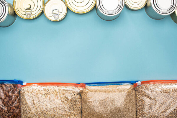 top view of cans and groats in zipper bags on blue background with copy space