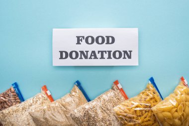 Makarna, fasulye ve iniltilerin üst görüntüsü mavi arka planda yiyecek bağışı kartıyla fermuar poşetlerinde.