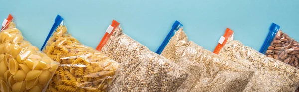 top view of pasta, beans and groats in zipper bags on blue background, food donation concept