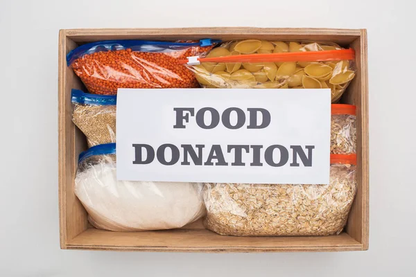 top view of pasta and groats in zipper bags in wooden box with food donation card on white background