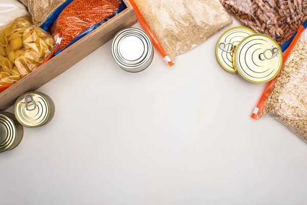 top view of cans and groats in zipper bags with wooden box on white background, food donation concept