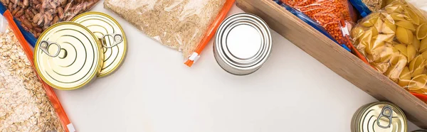 top view of cans and groats in zipper bags with wooden box on white background, food donation concept