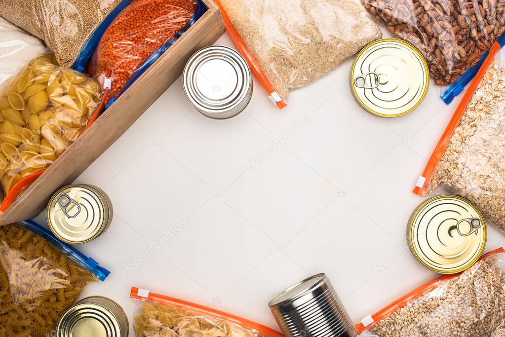 top view of cans and groats in zipper bags with wooden box on white background, food donation concept