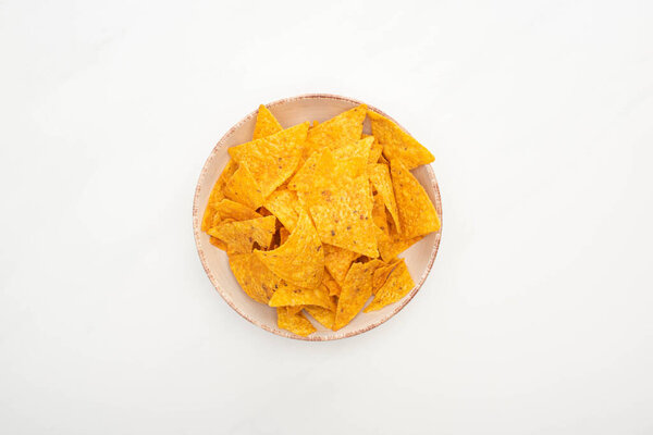 top view of crunchy corn nachos in bowl on white background