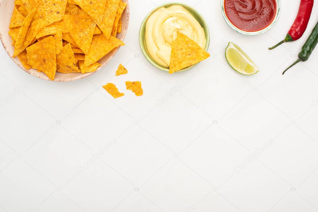 top view of corn nachos with lime, chili peppers, ketchup and cheese sauce on white background