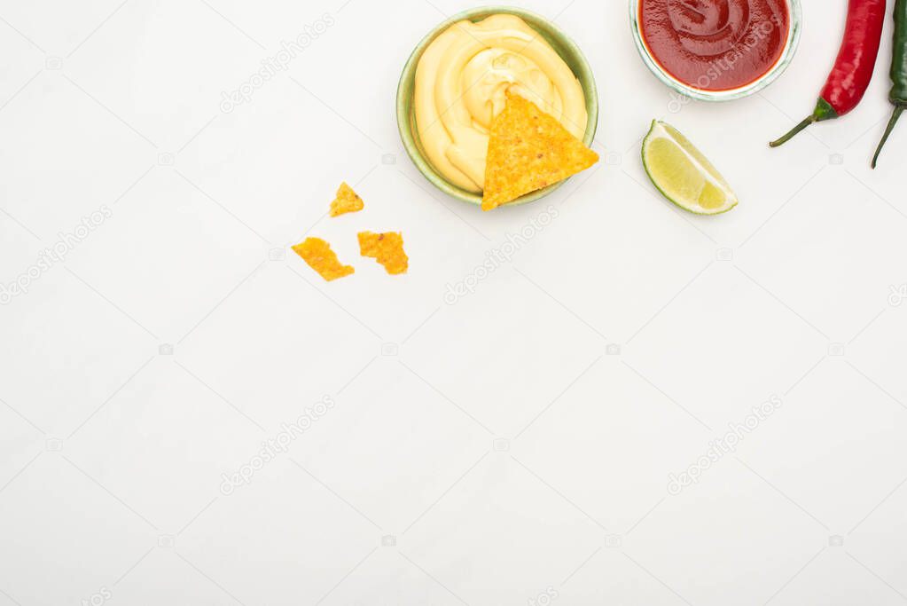 top view of corn nachos with lime, chili peppers, ketchup and cheese sauce on white background