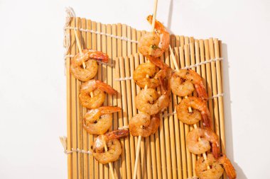 top view of prawns on skewers on bamboo mat on white background clipart