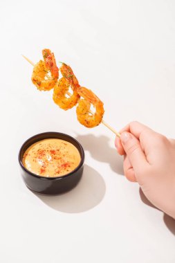 cropped view of woman holding tasty fried prawns on skewer near sauce on white background clipart