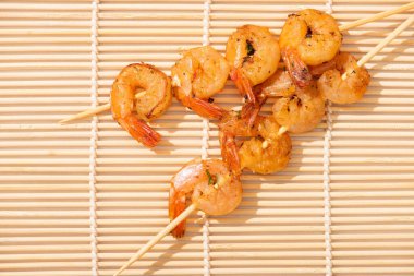 top view of tasty prawns on skewers on beige bamboo mat clipart