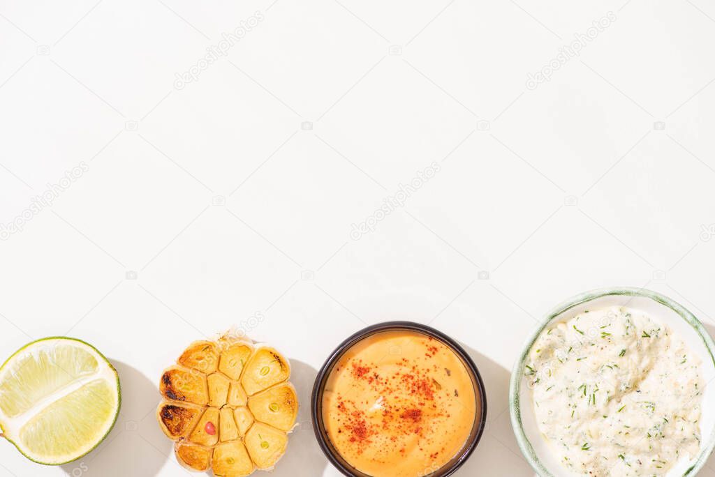 top view of garlic, lime and sauces on white background