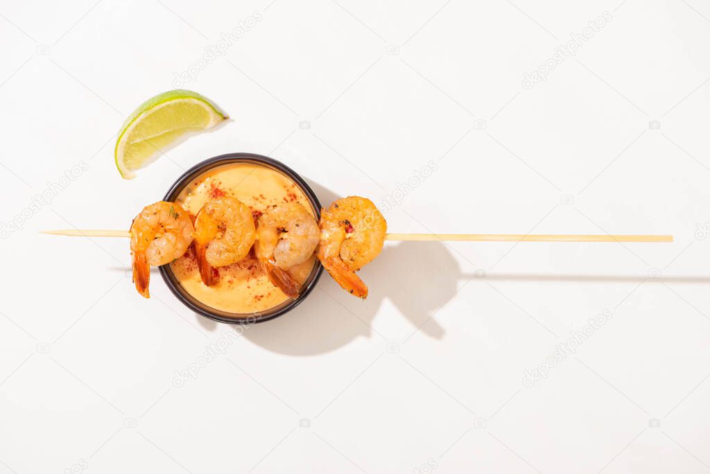 top view of delicious fried prawns on skewer with lime and sauce on white background