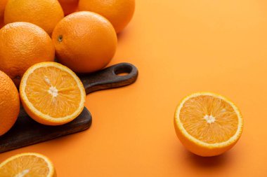 ripe delicious cut and whole oranges on wooden cutting board on colorful background clipart