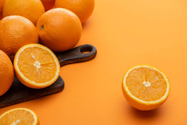 ripe delicious cut and whole oranges on wooden cutting board on colorful background